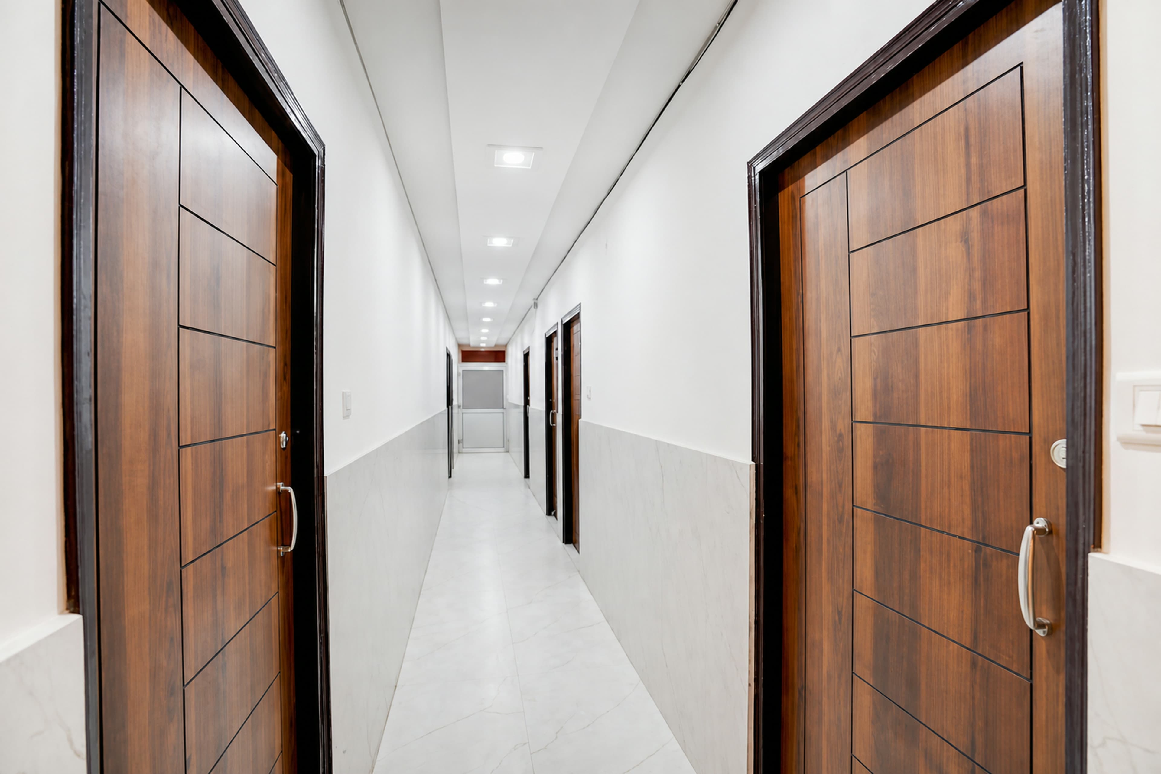 Bright, clean guest-room corridor with wooden doors and marble-tiled walls at Metro Club & Guest House, Lucknow