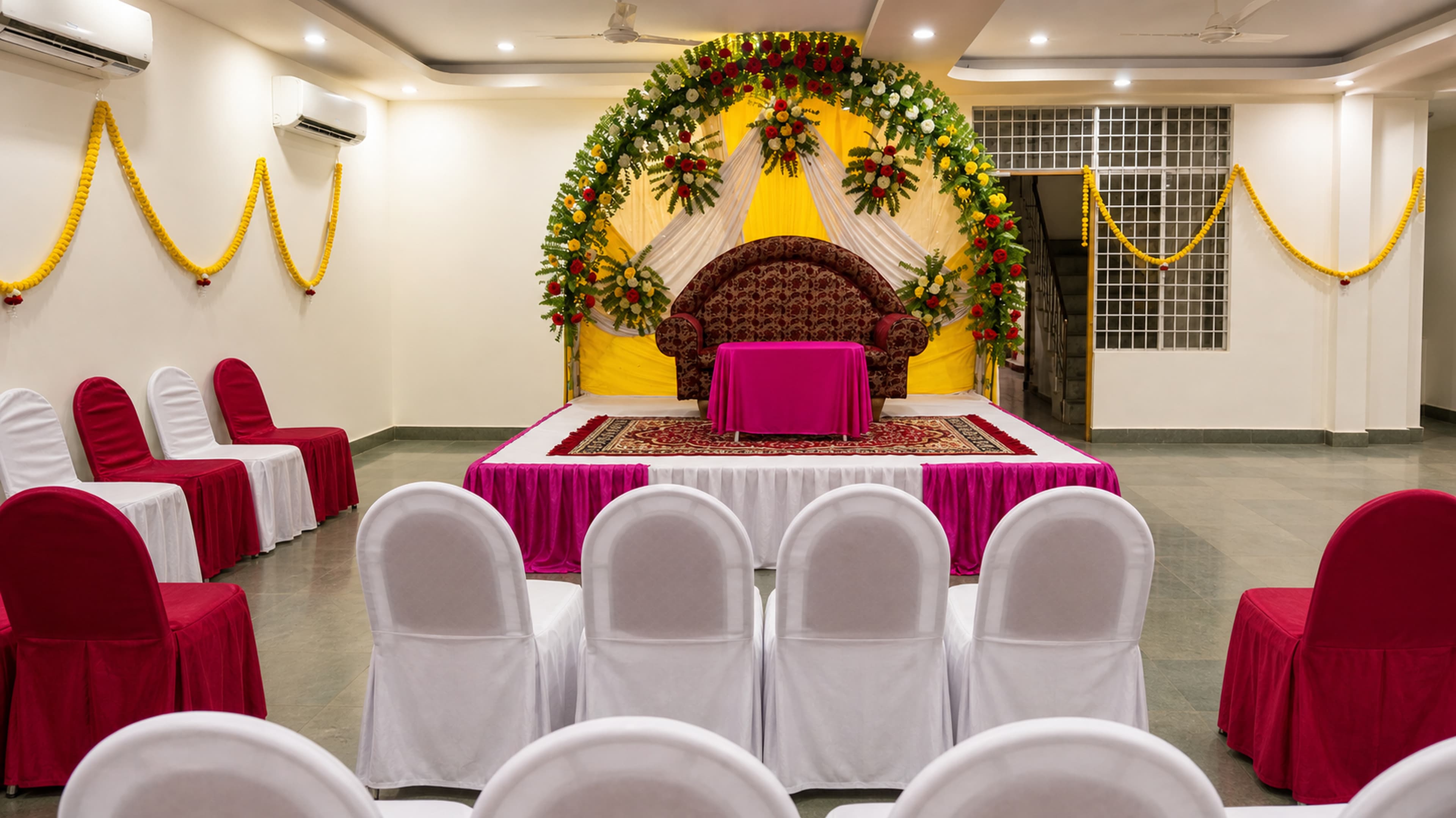 The banquet hall set for a function with a floral stage and rows of covered chairs