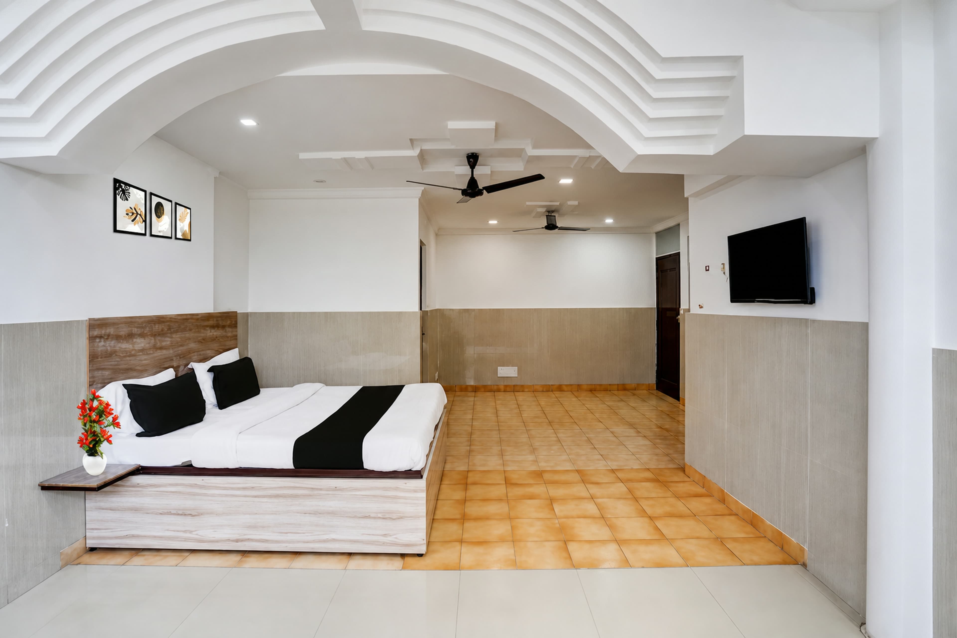 Spacious premium room with an arched ceiling, wooden bed, wall-mounted TV and tiled flooring